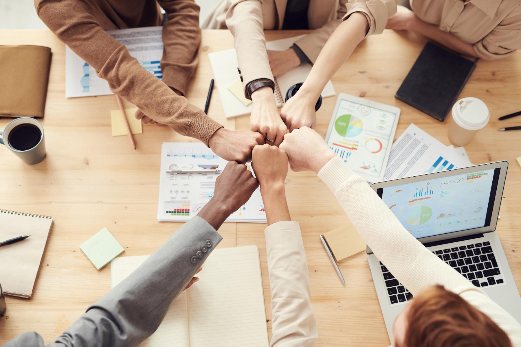 From Stress to Strength: How High-Performing Teams Build Sustainable Resilience 1 Team joining fists over a desk of charts, the unity resilience training aims for